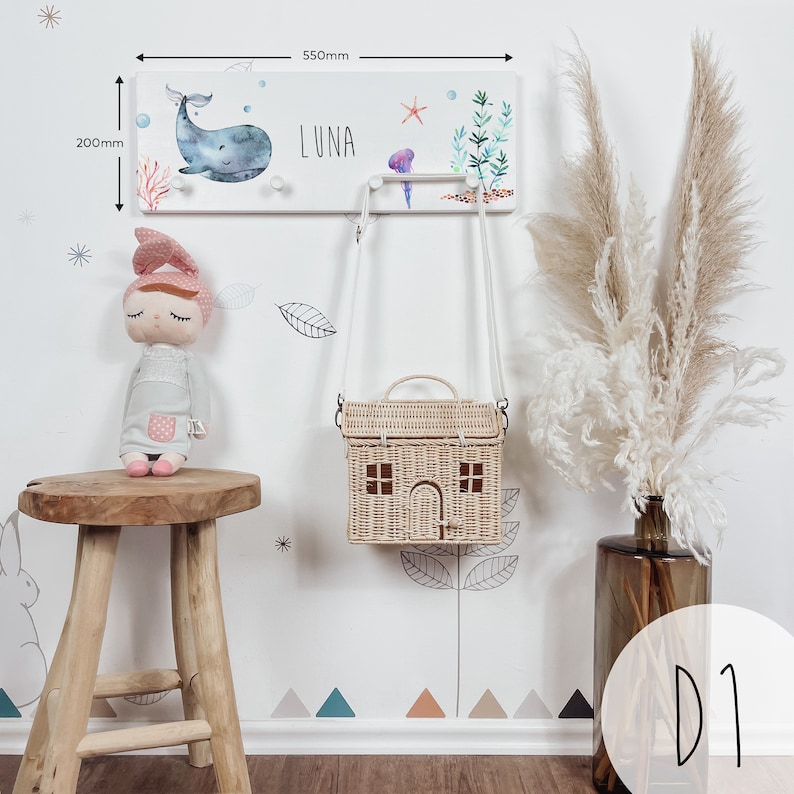 May include: White wooden coat rack with a whale, starfish, and seaweed design. The rack has two hooks and the name "LUNA" is written on it. The rack is 22 inches wide and 8 inches tall.