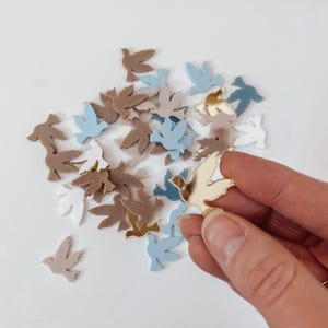 K&ouml;nnte beinhalten: Sortiment kleiner, taubenf&ouml;rmiger Acrylschnitte in verschiedenen Farben, darunter Gold, Wei&szlig;, Hellblau und Braun. Die Ausschnitte sind auf einer wei&szlig;en Oberfl&auml;che verstreut.