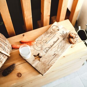 May include: A wooden serving tray with a star cutout and the text "For Dich, lieber Weihnachtsmann!"  The tray is decorated with drawings of carrots, a star, and a circle. There are two carrots, a glass of milk, and two cookies on the tray.