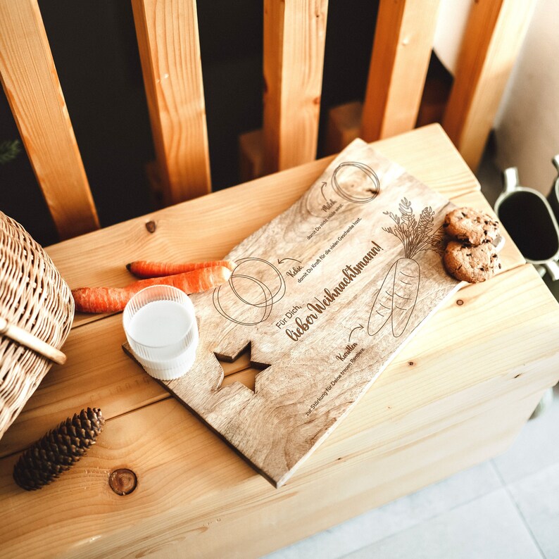 May include: A wooden serving tray with a star cutout and the text "For Dich, lieber Weihnachtsmann!"  The tray is decorated with drawings of carrots, a star, and a circle. There are two carrots, a glass of milk, and two cookies on the tray.