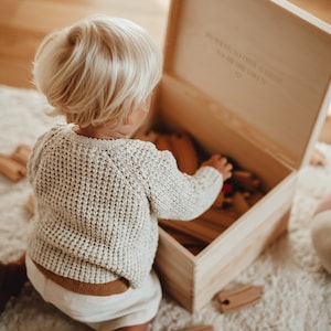 Ein kleiner Junge vor unserer Holzkiste mit Spielzeug drin. Im Innendeckel ein wunderschöner Spruch. Lass dein Herz dich führen.  In der Kiste können auch hochwertige Erinnerungen aufbewahrt werden.