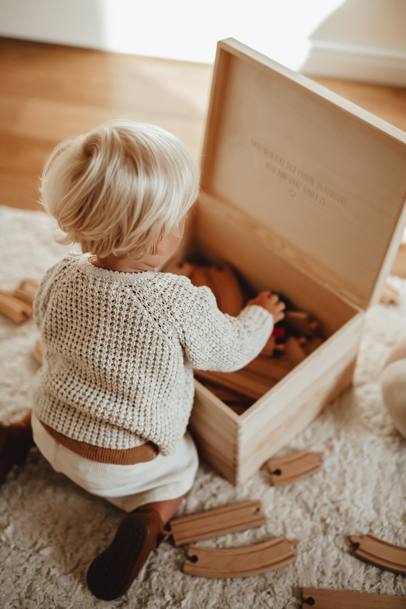 Ein kleiner Junge vor unserer Holzkiste mit Spielzeug drin. Im Innendeckel ein wunderschöner Spruch. Lass dein Herz dich führen.  In der Kiste können auch hochwertige Erinnerungen aufbewahrt werden.