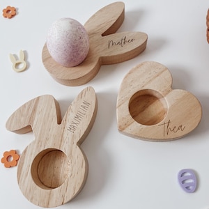 Può includere: Tre porta uova di Pasqua in legno. Uno è a forma di coniglio con il nome Maximilian, un altro è a forma di coniglio con il nome Matteo e l'ultimo è a forma di cuore con il nome Thea.