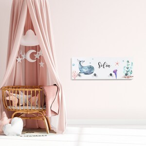 May include: A white wooden wall-mounted coat rack with a whale and ocean-themed design. The rack has four hooks and the name "Sofia" is written on it.