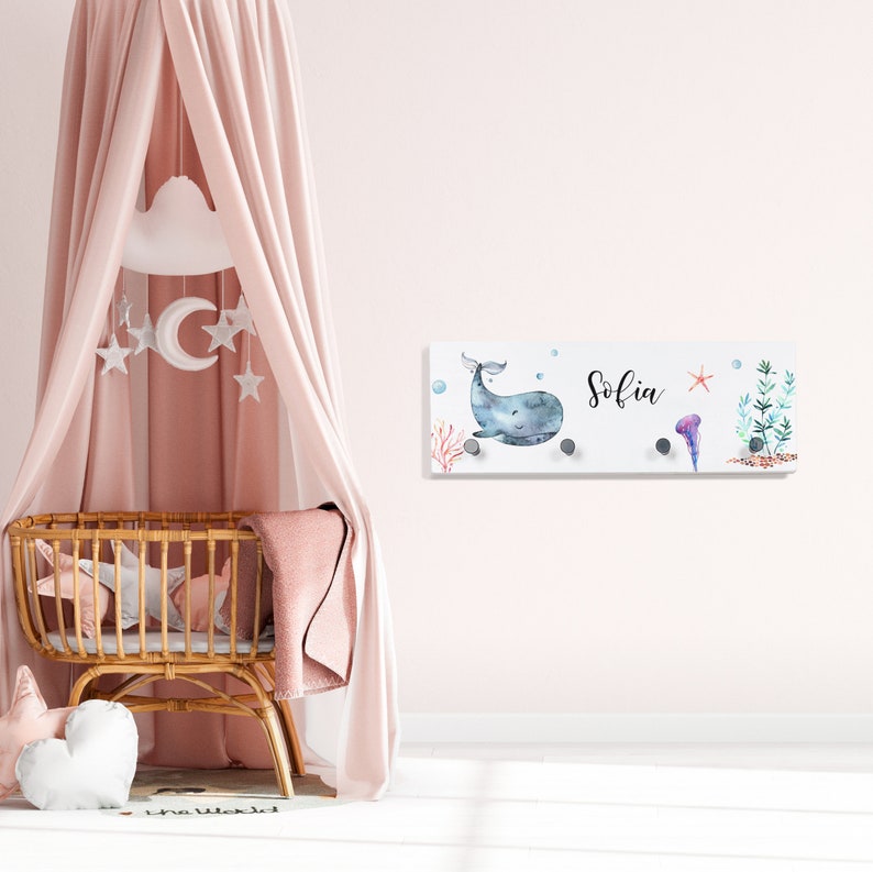 May include: A white wooden wall-mounted coat rack with a whale and ocean-themed design. The rack has four hooks and the name "Sofia" is written on it.