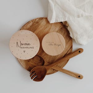 Könnte beinhalten: Holz-Küchenutensilien-Set mit zwei runden Untersetzern mit Text, einem Holzserviertablett und zwei Holzservierlöffeln. Auf einem Untersetzer steht "Nerven Nahrung" und auf dem anderen "It's the little things."
