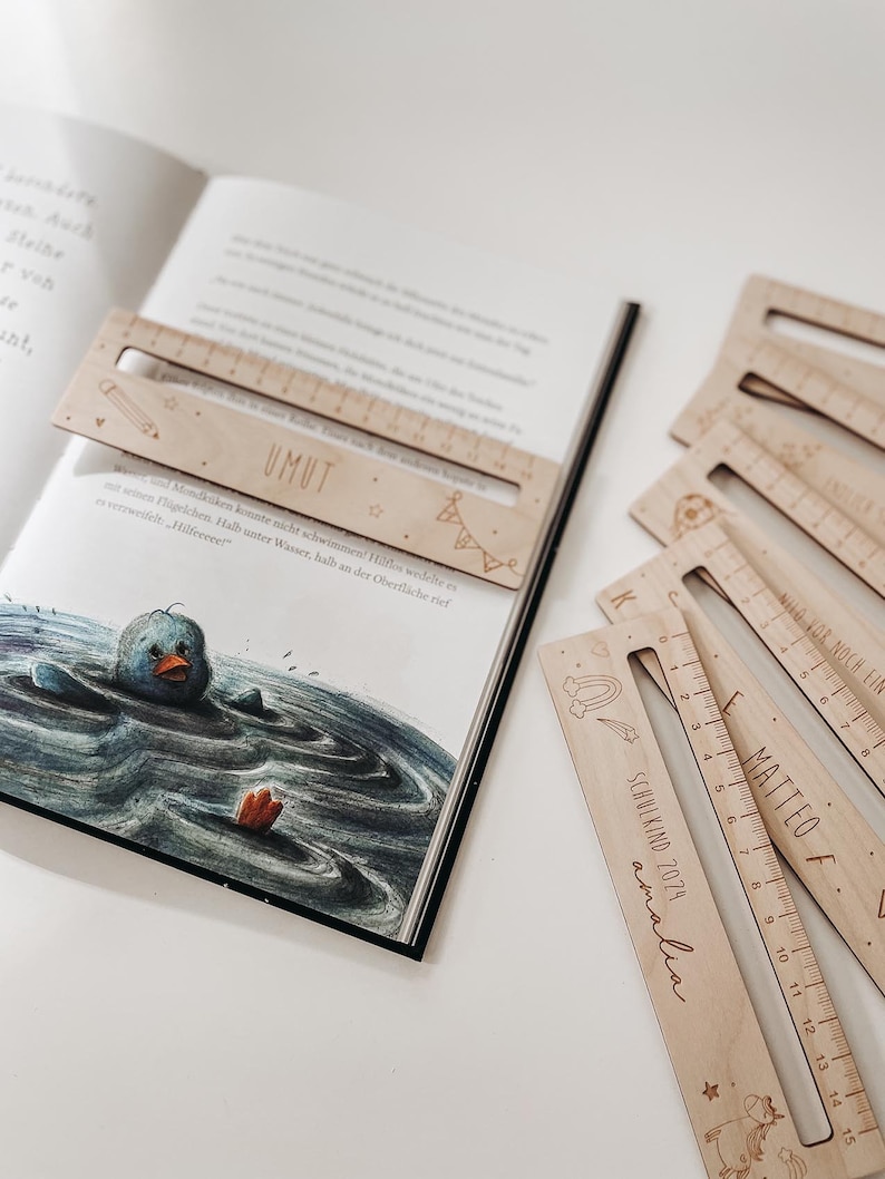 K&ouml;nnte beinhalten: Ein Set aus sieben Holzlinealen mit einem Regenbogen-, Stern- und Einhorn-Design. Die Lineale sind mit den Namen "UMUT" und "MATTEO F." sowie dem Text "SCHULKIND 2029 amalia" personalisiert.