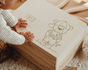 May include: A wooden toy chest with a light wood finish. The lid has a gold inscription that reads "Theo 2023" and features a cartoon bear wearing a baseball cap and overalls.