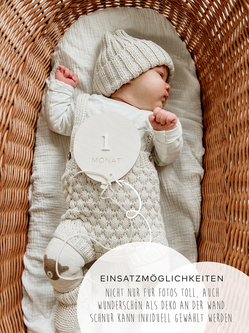 Puede incluir: Un c&iacute;rculo de madera blanco con el n&uacute;mero "1" y la palabra "MONAT" en &eacute;l. Un beb&eacute; est&aacute; acostado en una cesta de mimbre con un gorro de punto y un atuendo de punto. El texto "EINSATZM&Ouml;GLICHKEITEN" es visible en la parte inferior de la imagen.  NICHT NUR F&Uuml;R FOTOS TOLL, AUCH WUNDERSCH&Ouml;N ALS DEKO AN DER WAND. SCHNUR KANN INVIDUELL GEW&Auml;HLT WERDEN.