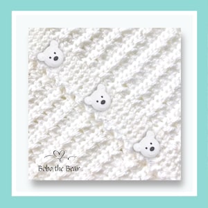 May include: A white crocheted blanket with three white bear-shaped buttons. The blanket has a textured pattern. The text "Bobo the Bear" is in the lower left corner.