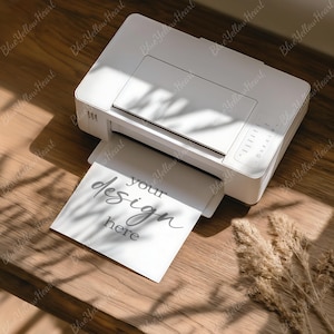 May include: A white printer with a printed sheet of paper that says "your design here". The printer is on a wooden surface with a dried plant and shadows.