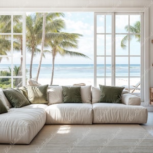 May include: A white sectional sofa with green throw pillows sits in a living room with large windows overlooking a beach scene. The room has a wooden shelf with decorative items and books.
