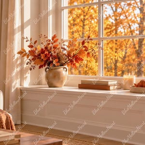 May include: A ceramic vase filled with orange and red autumn leaves sits on a window ledge next to a stack of books, a candle, and a wooden tray holding small pumpkins. The scene is set against a large window with a view of fall foliage.