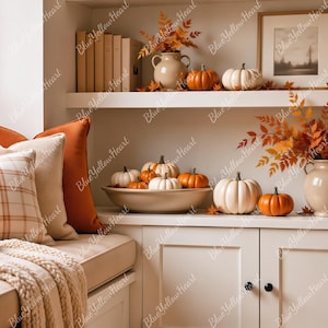May include: A cozy window seat featuring orange and cream plaid pillows, a textured throw blanket, and a ceramic vase with autumn leaves. Built-in shelves display books, framed art, ceramic vases, and various orange and white pumpkins.