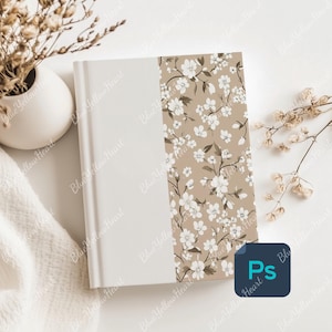 May include: A white notebook with a beige floral design on the spine. The notebook is on a white surface with dried flowers.