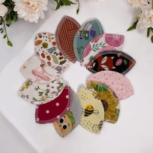 May include: A set of 12 reusable makeup remover pads with various colorful patterns, including floral, geometric, and animal prints. The pads are arranged in a circle on a white surface.