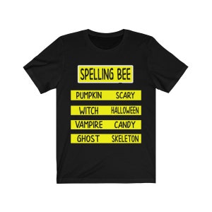 May include: Black t-shirt with a yellow sign that says "Spelling Bee" and lists Halloween words like "pumpkin", "scary", "witch", "halloween", "vampire", "candy", "ghost", and "skeleton".