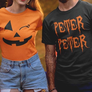 May include: A couple wearing matching Halloween shirts. The woman's shirt is orange with a black winking jack-o'-lantern face. The man's shirt is black with the word "PETER" written in orange, twice, in a gothic font.