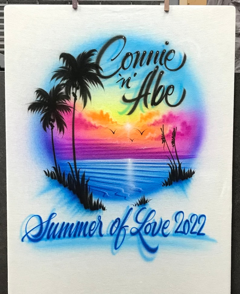 May include: A white canvas with a colorful airbrushed design of a sunset over the ocean with palm trees. The text "Connie 'n Abe Summer of Love 2022" is written in blue cursive.