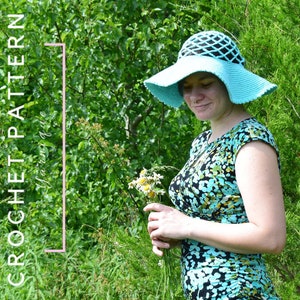 May include: A light blue crochet sun hat with a wide brim and a crocheted design. The hat is worn by a person in a floral print dress.