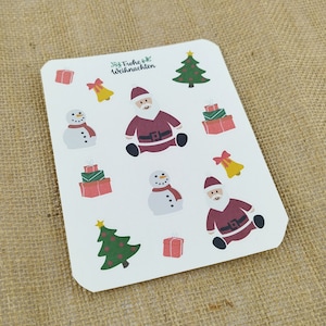 Könnte beinhalten: Ein Bogen mit weihnachtlichen Aufklebern mit Motiven von Weihnachtsmann, Schneemännern, Weihnachtsbäumen, Geschenkboxen und Glocken. Die Aufkleber sind in Rot, Grün, Weiß und Gelb gehalten. Der Text "Frohe Weihnachten" ist ebenfalls vorhanden.