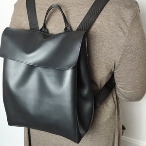 May include: A black faux leather backpack with adjustable straps. The backpack has a flap closure and a single compartment.
