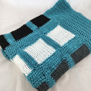 May include: A crocheted blanket with a checkered pattern in teal, white, black, and grey.