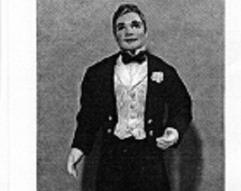 May include: A black and white image of a doll dressed in formal attire. The doll wears a black tuxedo jacket, black pants, a white vest, and a bow tie. The doll is standing on a white circular base.