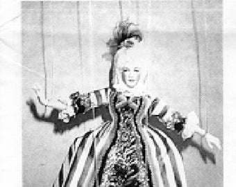 May include: A vintage doll in a period costume, featuring a white wig, a ruffled collar, and a striped gown with a decorative bodice. The doll's arms are outstretched, and the dress has a wide skirt with a dark hem.