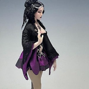 May include: A gothic-style doll with a black and purple ensemble. The doll has black hair, a black jacket with lace sleeves, and a purple skirt. She wears black high heels and stands on a black base.