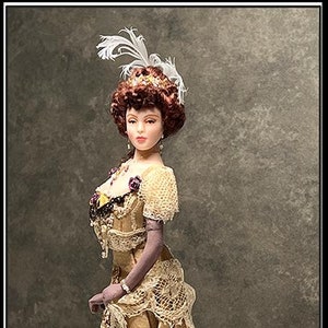 Può includere: Bambola dettagliata in un abito dorato in stile vintage, ornata di pizzo e dettagli viola. La bambola ha i capelli rossi e un copricapo di piume. L'abito ha una gonna lunga e uno strascico. La bambola è in piedi su uno sfondo grigio. Firmato "Agnes".