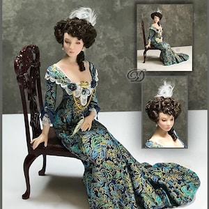 Puede incluir: Una muñeca en miniatura con un vestido estampado en verde azulado y dorado, sentada en una silla de madera oscura. La muñeca tiene cabello rizado oscuro, una pluma blanca en el cabello y un rostro detallado. El vestido presenta adornos de encaje y un collar dorado. Imágenes adicionales de la muñeca en el fondo.