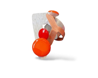 Puede incluir: Un anillo con una base cuadrada plateada texturizada, una banda de metal cobrizo y dos acentos circulares naranjas lisos y brillantes. El diseño incorpora un círculo naranja más grande en la parte inferior y uno más pequeño encima.