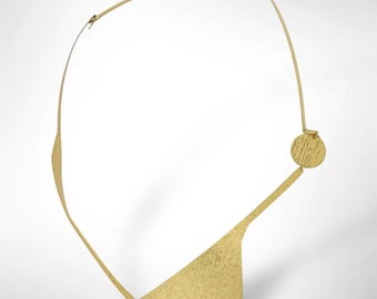 Pode incluir: Um colar dourado com um design abstrato único. Apresenta uma parte superior curva, um pendente triangular texturizado e um detalhe circular. O metal tem uma textura martelada, dando-lhe um aspeto artesanal. Uma peça de destaque.