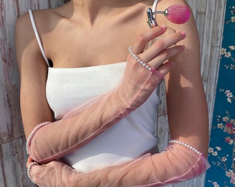 May include: A pair of pink sheer gloves with pearl embellishments. The gloves are worn on both hands and are shown against a white background.