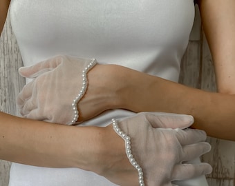 Könnte beinhalten: Ein Paar weiße, durchsichtige Handschuhe mit Perlenbesatz. Die Handschuhe sind aus einem zarten Stoff gefertigt und haben einen gewellten Rand.