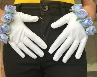 May include: White gloves adorned with light blue and purple floral accents. The gloves are made of a smooth, opaque material. The floral accents are clustered around the wrist area. The background includes black pants and a yellow top.