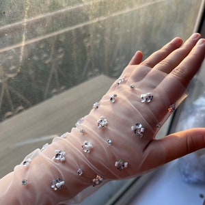 May include: White sheer gloves with delicate white and silver embellishments. The gloves are made of a fine mesh fabric and have a subtle sparkle.