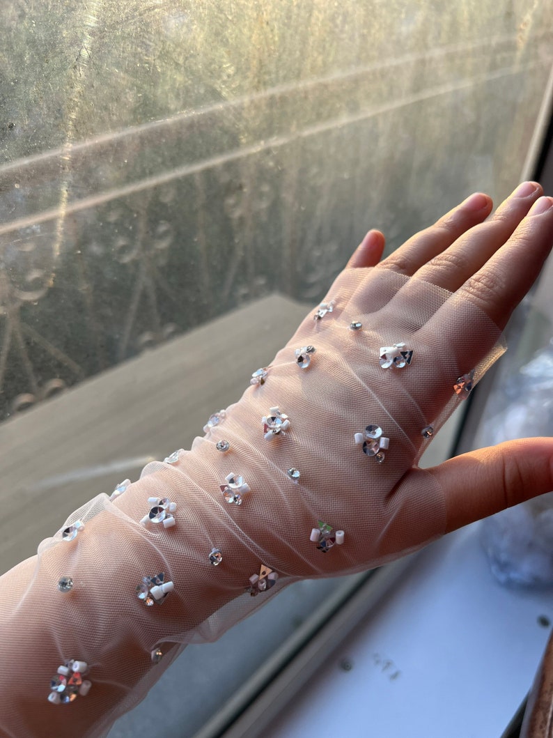 May include: White sheer gloves with delicate white and silver embellishments. The gloves are made of a fine mesh fabric and have a subtle sparkle.