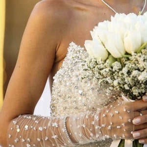 May include: A bride wearing a white strapless gown with a beaded bodice and a white veil. She is holding a bouquet of white tulips and white flowers.