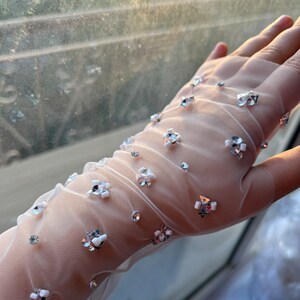May include: White sheer gloves with silver and white embellishments. The gloves are made of a delicate mesh fabric and have a subtle sparkle.