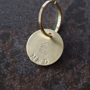 May include: A gold-toned keychain with a round tag featuring a house icon and the engraved text "M & D".