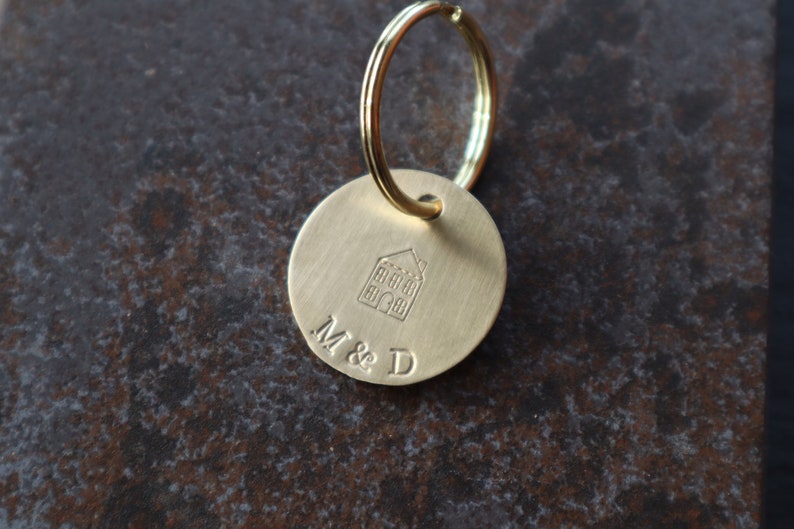 May include: A gold-toned keychain with a round tag featuring a house icon and the engraved text "M & D".