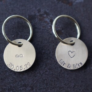 May include: Two brass keychains with round tags. One tag has an infinity symbol and the date 30.05.22 engraved on it. The other tag has a heart and the text "Mr & Mrs" engraved on it.