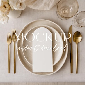 May include: A table setting with a white plate, gold cutlery, and a white card. The plate is set on a beige tablecloth, with a glass and flowers in the background. The text "MOCKUP instant download" is on the plate.