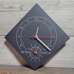 Puede incluir: Un reloj de pizarra negra en forma de diamante con números y manecillas blancas. La esfera del reloj tiene un indicador de marea en la parte inferior, con las palabras "High Tide" y "Low Tide". Las manecillas del reloj son doradas con un segundero rojo.