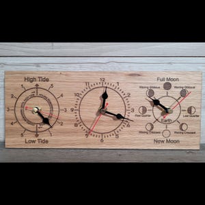 May include: A rectangular wooden wall clock featuring three circular dials. The left dial tracks tide levels, the centre dial displays standard time, and the right dial shows moon phases. Each dial has black hands and engraved text labels.