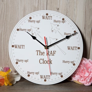 Peut inclure: Une horloge ronde blanche avec du texte brun qui indique "The RAF Clock". Le cadran de l'horloge a un motif d'avions avec les mots "Hurry up!" et "Wait!" autour du cadran de l'horloge.