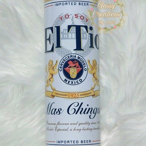 May include: A white and yellow insulated tumbler with a design of a beer can. The can features the text "El Tio" and "Mas Chingon" with a logo for Cerveceria Modelo. The text "Imported Beer" appears twice on the tumbler.