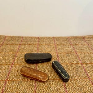 Könnte beinhalten: Drei Vintage-Brillenetuis. Eines ist schwarz, eines ist hellbraun und das dritte ist dunkelbraun mit einer strukturierten schwarzen Oberseite. Die Etuis sind rechteckig und geschlossen, zum Schutz von Brillen.